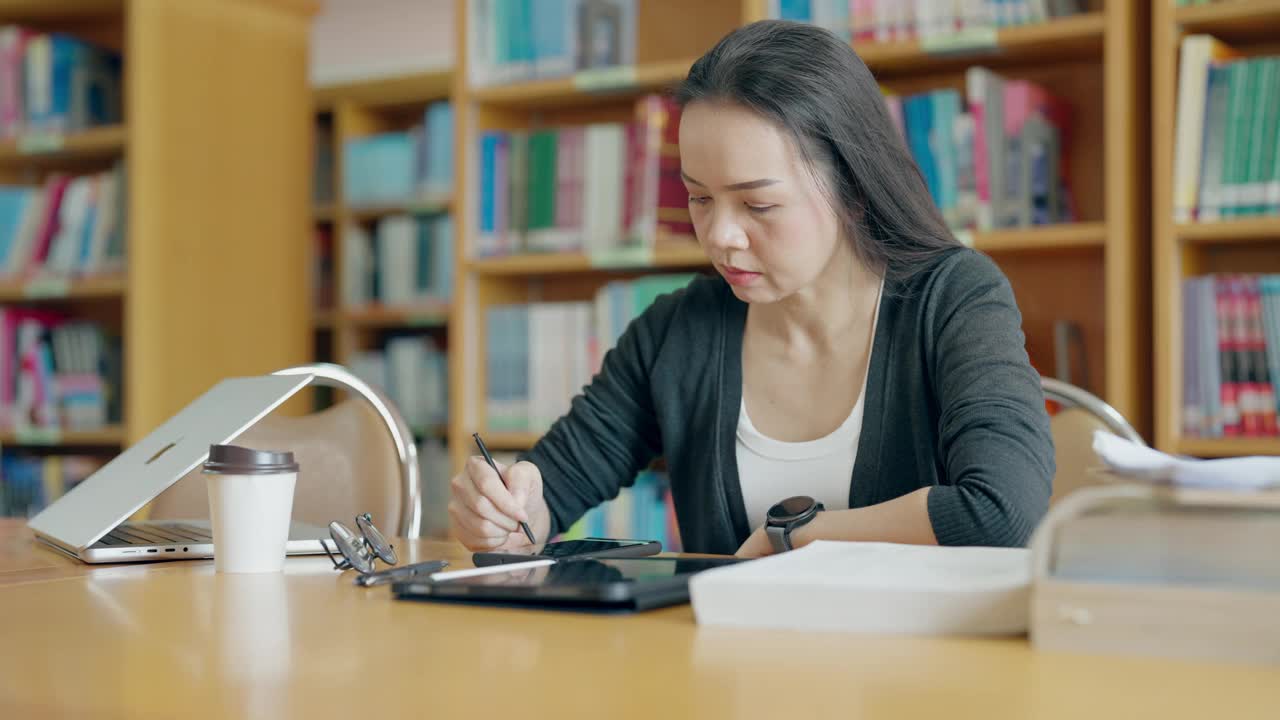 一个女人坐在图书馆的桌子旁，在写字板上写字视频素材