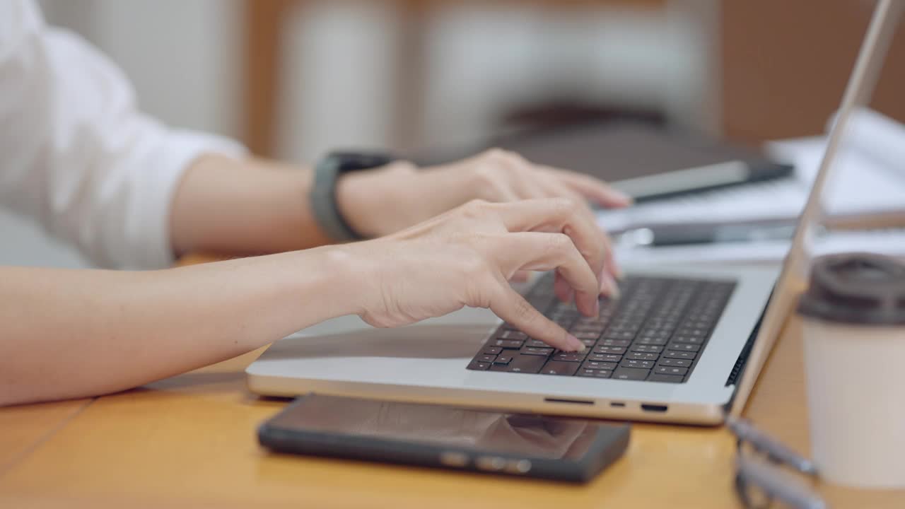 一位女士正在用手机在笔记本电脑上打字视频素材