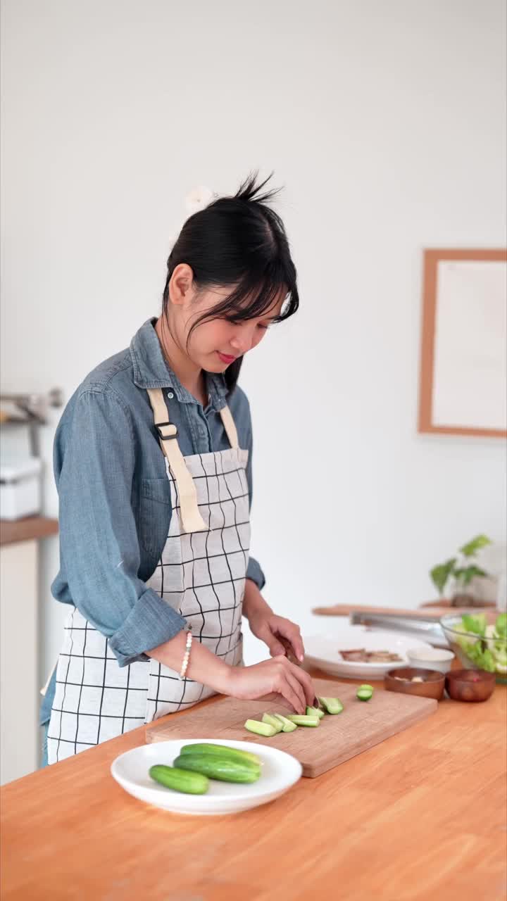 一位亚洲妇女正在家里的厨房里切黄瓜，作为亚洲菜的原料视频素材