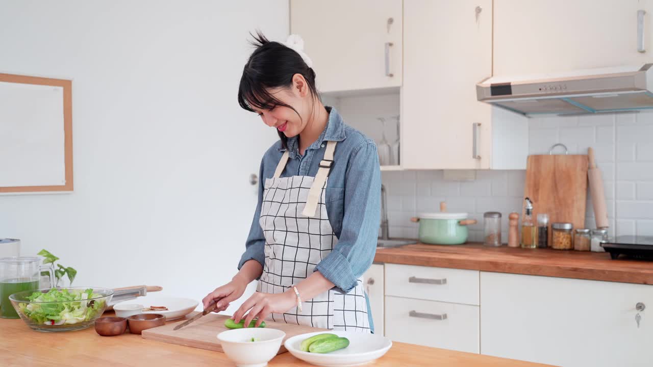 一位亚洲妇女正在家里的厨房里切黄瓜，作为亚洲菜的原料视频素材