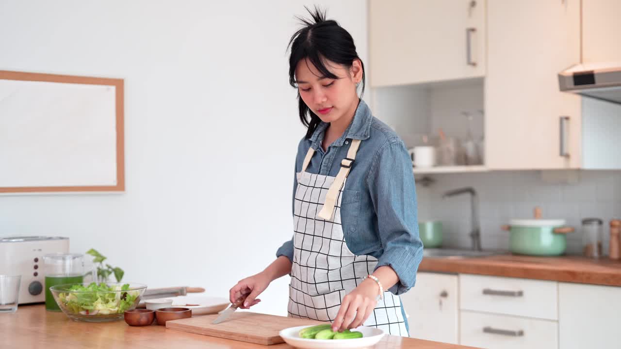 一位亚洲妇女正在家里的厨房里切黄瓜，作为亚洲菜的原料视频素材