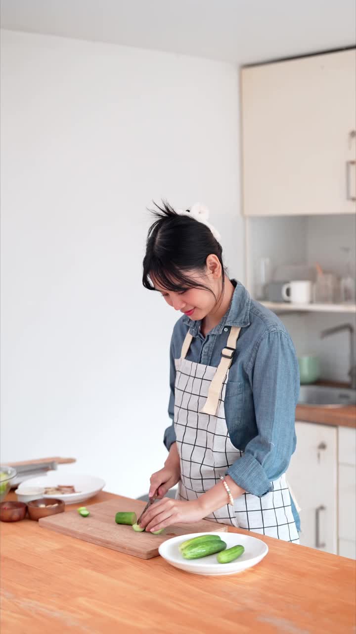 一位亚洲妇女正在家里的厨房里切黄瓜，作为亚洲菜的原料视频素材