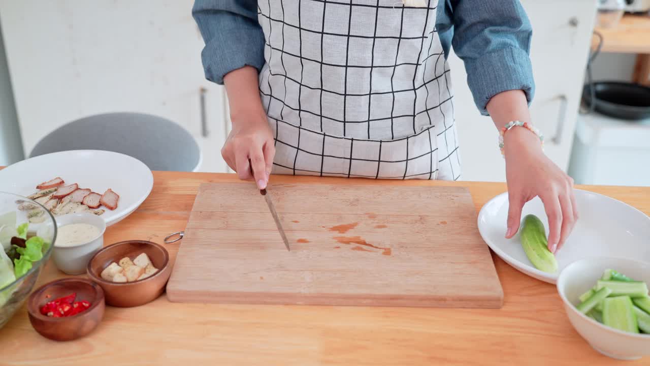 一位亚洲妇女正在家里的厨房里切黄瓜，作为亚洲菜的原料视频素材