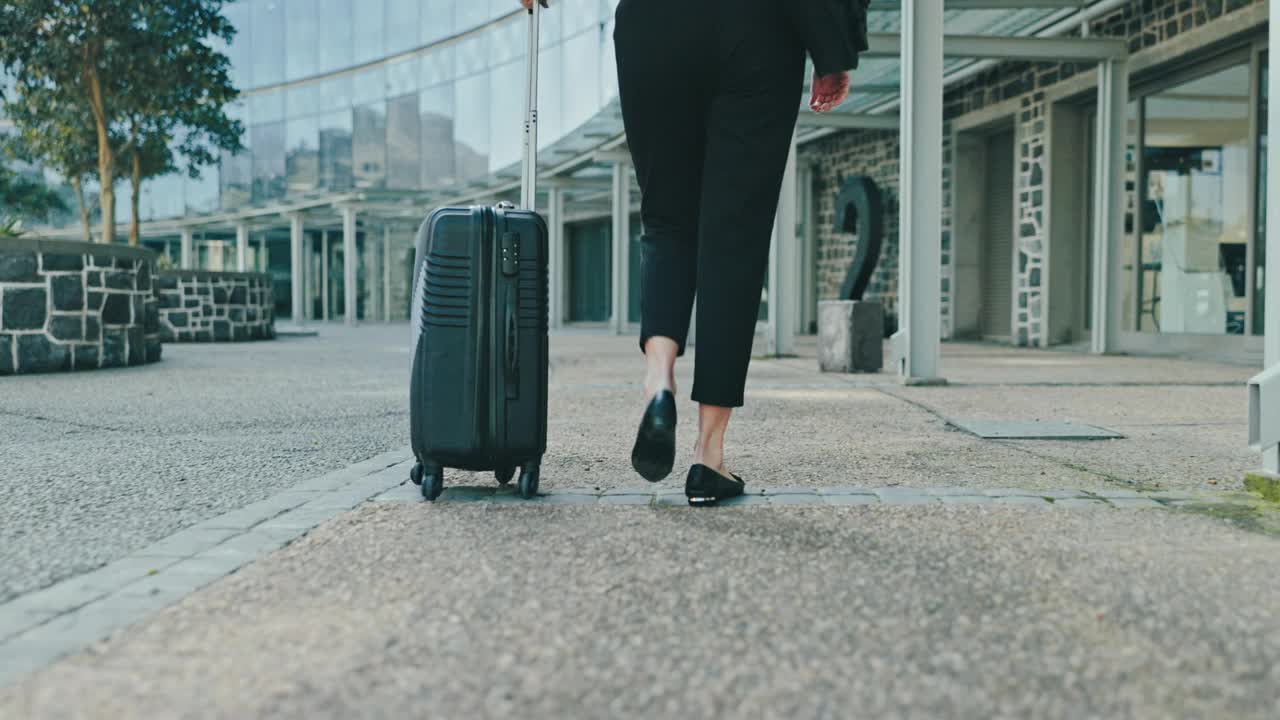 背起行李箱，一位商务女性走到机场进行国际旅行或出差。大楼，行李和一名专业员工站在城市的人行道上，准备搭乘公司航班视频素材