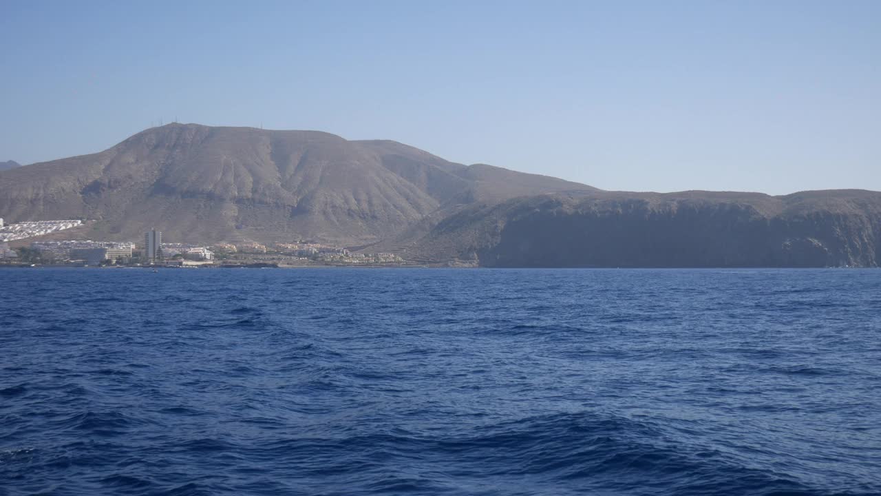 特内里费岛从海上。平静的蓝色海水通向崎岖的山地景观，海岸建筑在阳光下闪闪发光，非常适合宁静的自然主题视频素材