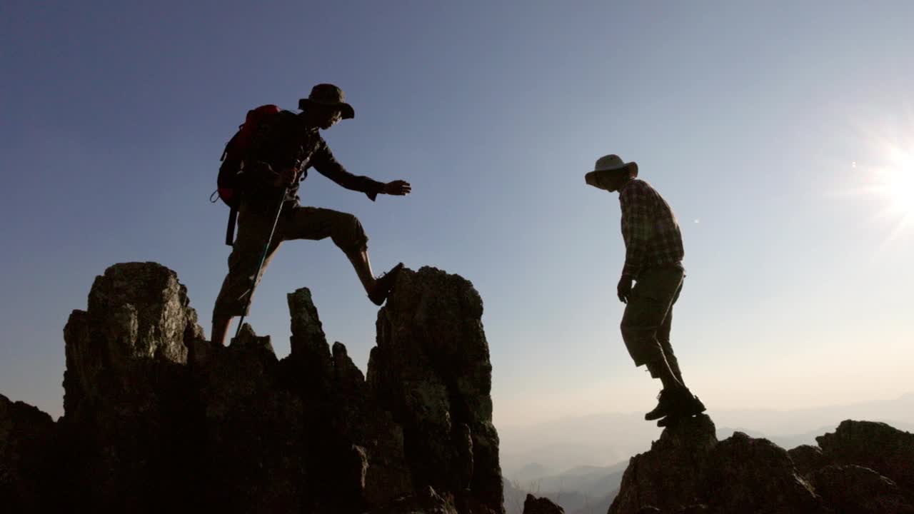 日出时人们互相帮助爬山。伸出援手，积极健康的生活方式理念。帮助和成功的概念，领导的概念，团队合作。视频素材