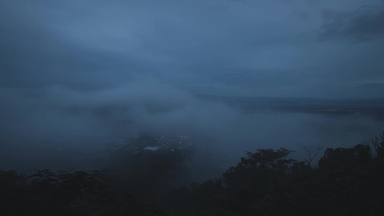 薄雾在夜幕降临前在城市上空飘过。雾笼罩着城市，城市笼罩在雾中。放大。视频下载