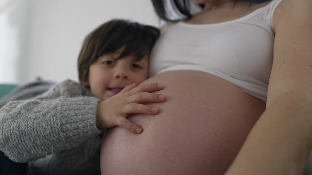 小男孩抚摸孕妈妈肚子的温柔瞬间，感受小弟弟的心跳，象征孕后期的母爱视频素材