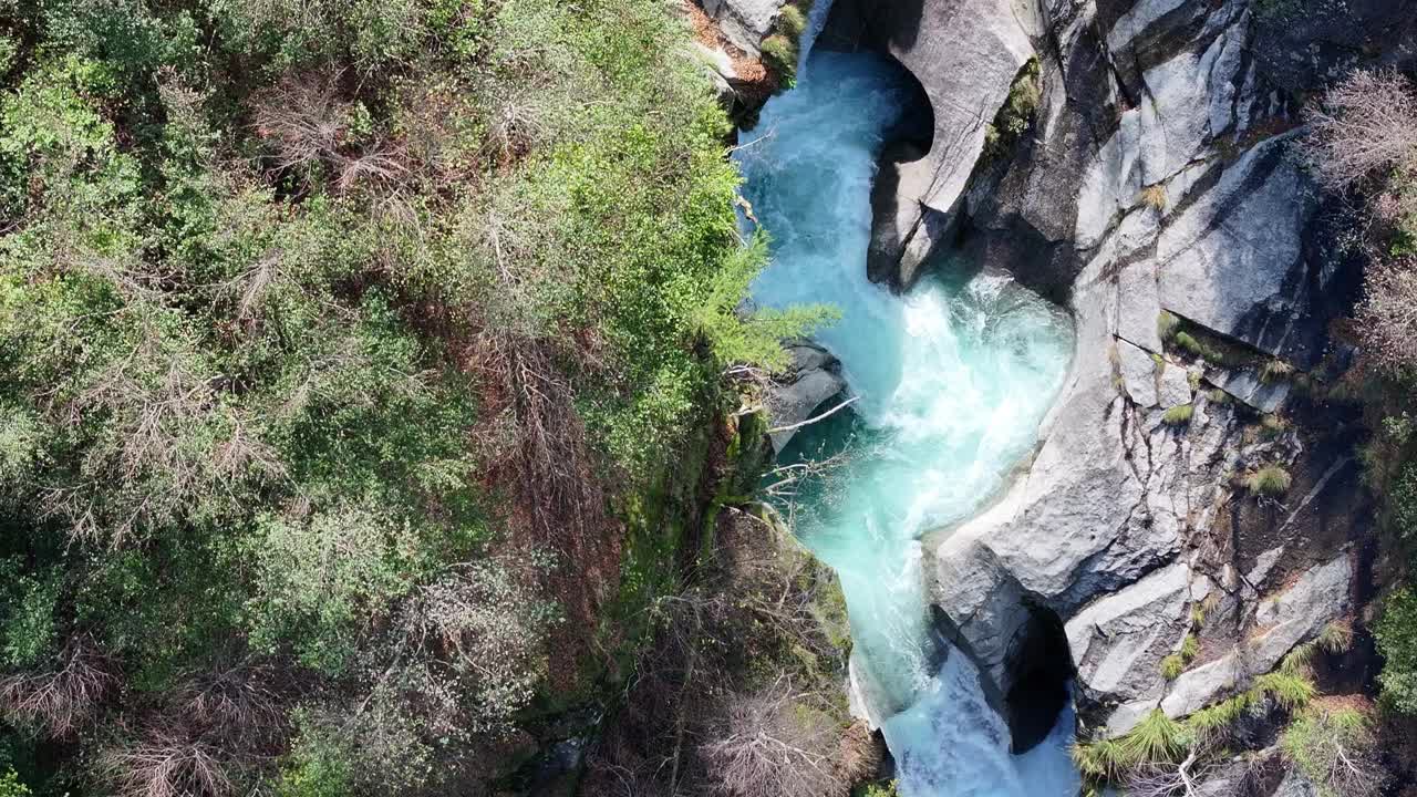 一个充满活力的绿松石瀑布雕刻通过岩石地形周围的郁郁葱葱的绿色植物，鸟瞰图视频素材