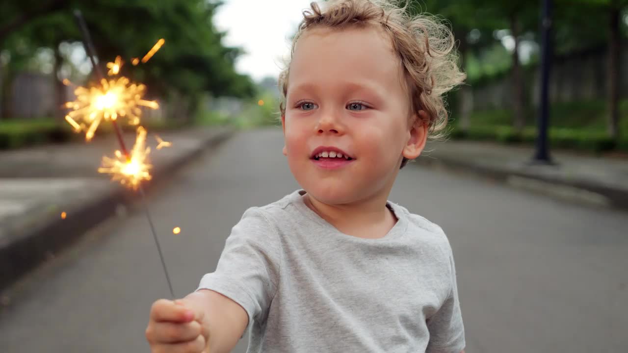 年幼的孩子手持烟花棒，指着两个火苗，拍下了肖像视频素材