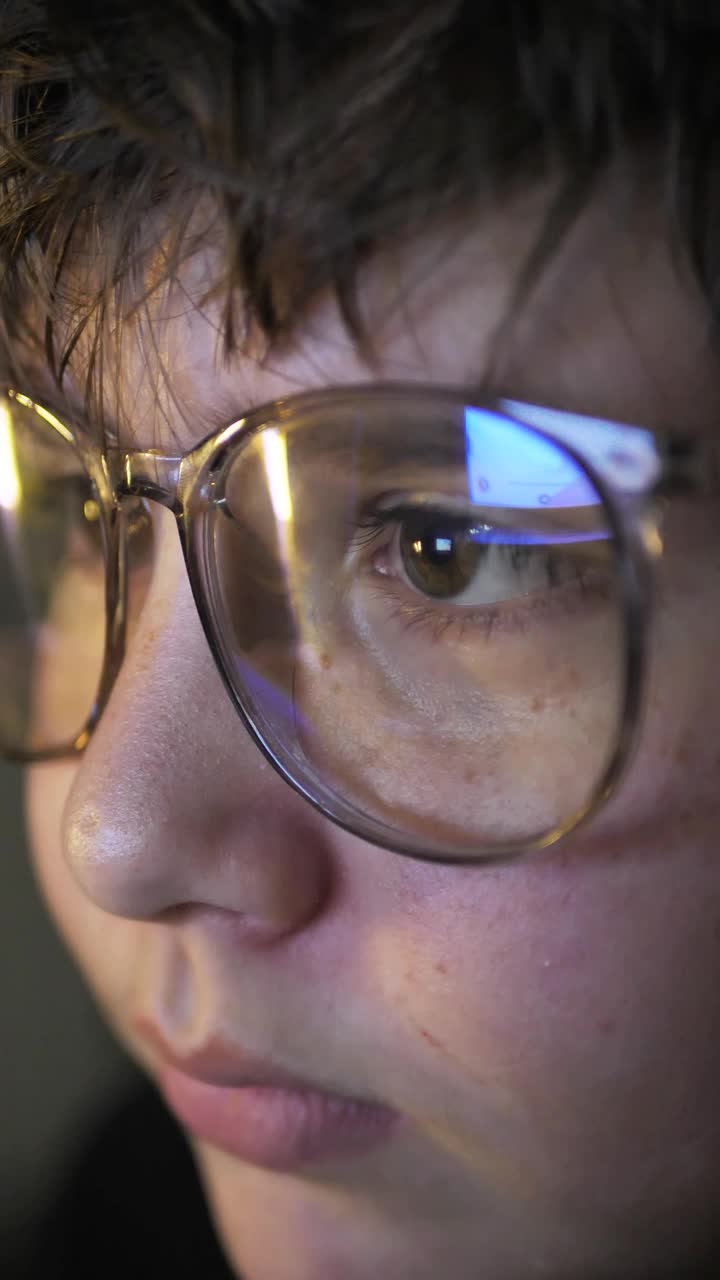 一个十几岁的男孩，戴着大眼镜，晚上在显示器前聊天。聪明的11岁男孩在玩网络游戏。儿童远程在线教育。视频素材