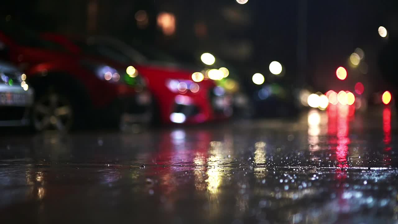 夜城暴雨的大气视频。大雨和汽车从低洼处经过的水坑溅起的水花。在街灯的照耀下，大雨滴落在人行道上视频下载