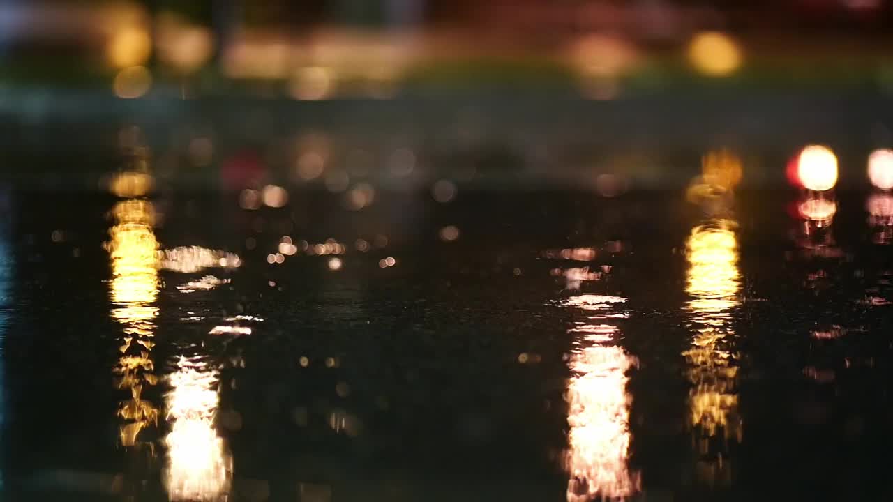 夜城暴雨的大气视频。大雨和溅起的水坑从低点拍摄。在街灯的照耀下，大雨滴落在人行道上。视频素材