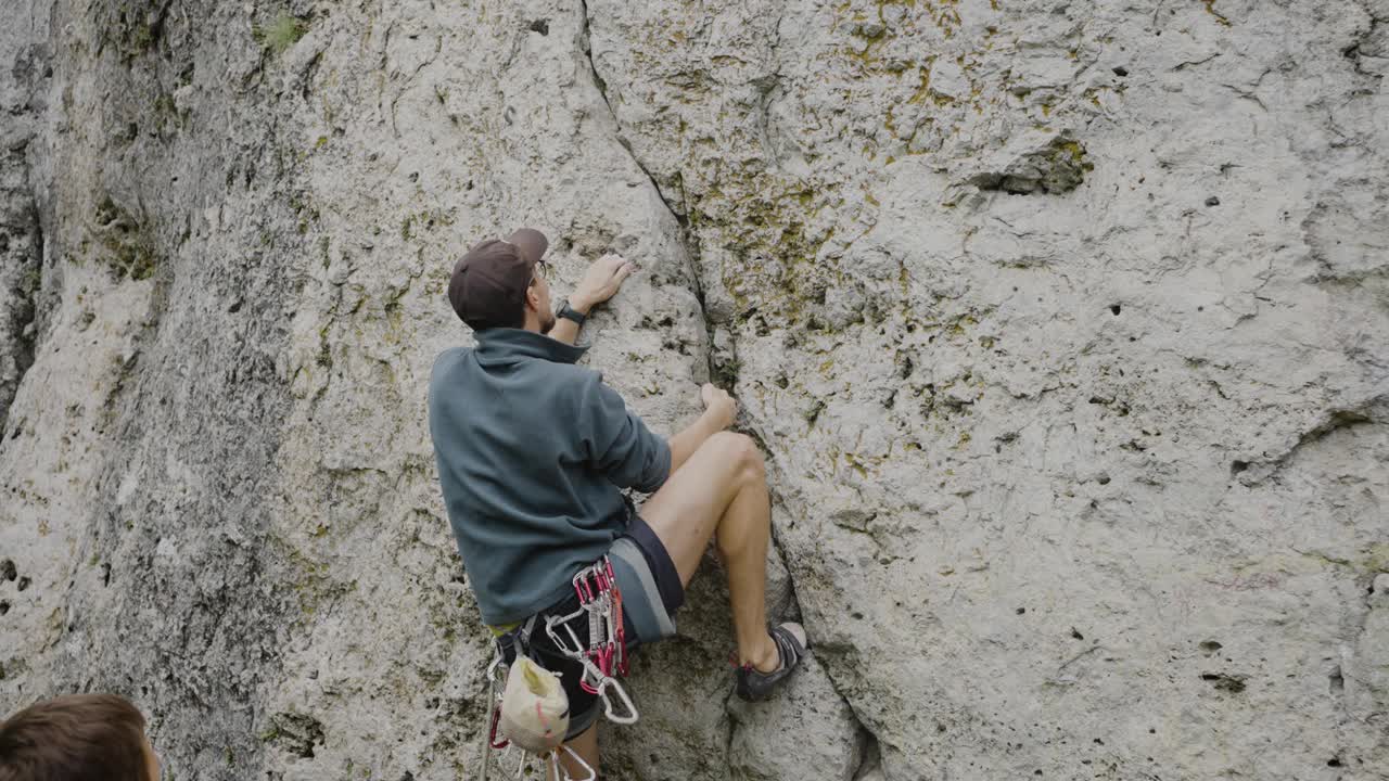 一名登山者带着白垩包和背带，在陡峭的岩壁上伸展身体准备下一步。视频素材