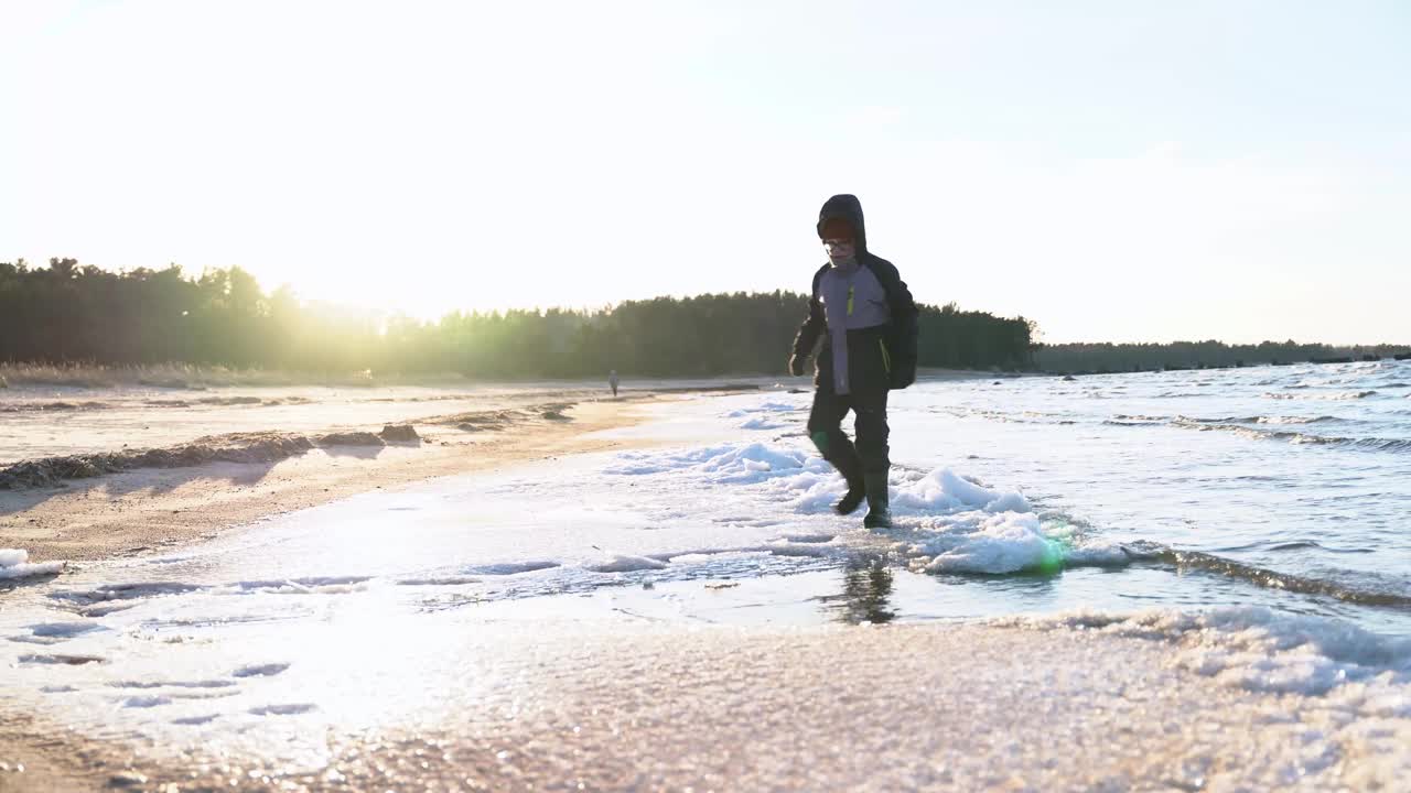 小男孩在海湾边的冬季沙滩上快乐地玩着浮冰和雪视频素材