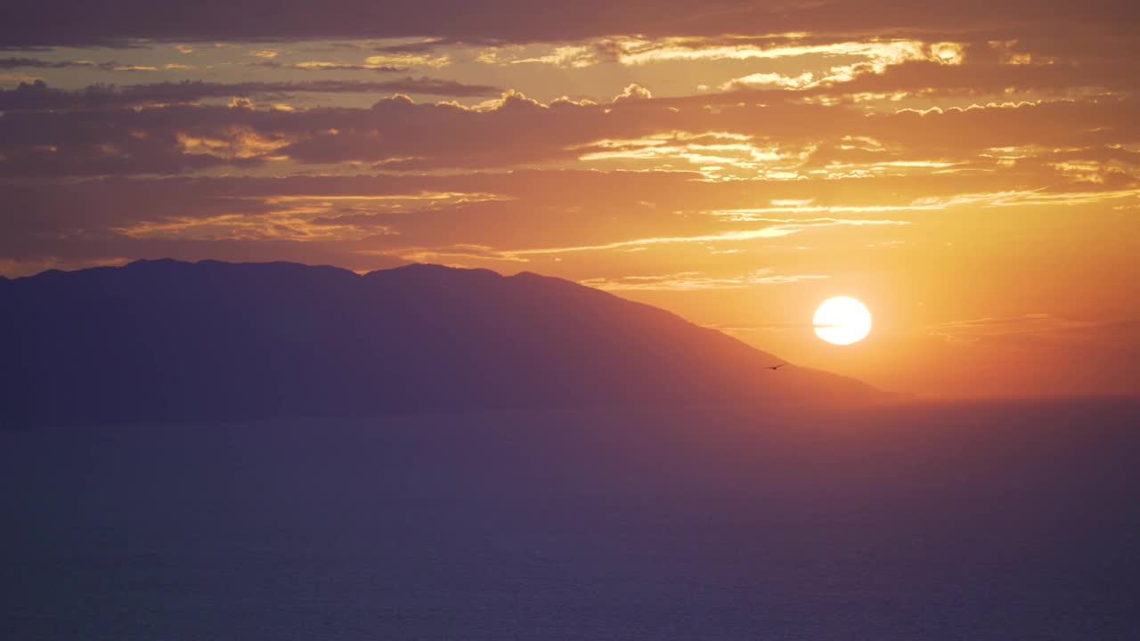 夕阳落在山后的海洋里，天空是金色的，云彩在移动，场景逐渐变黑视频素材