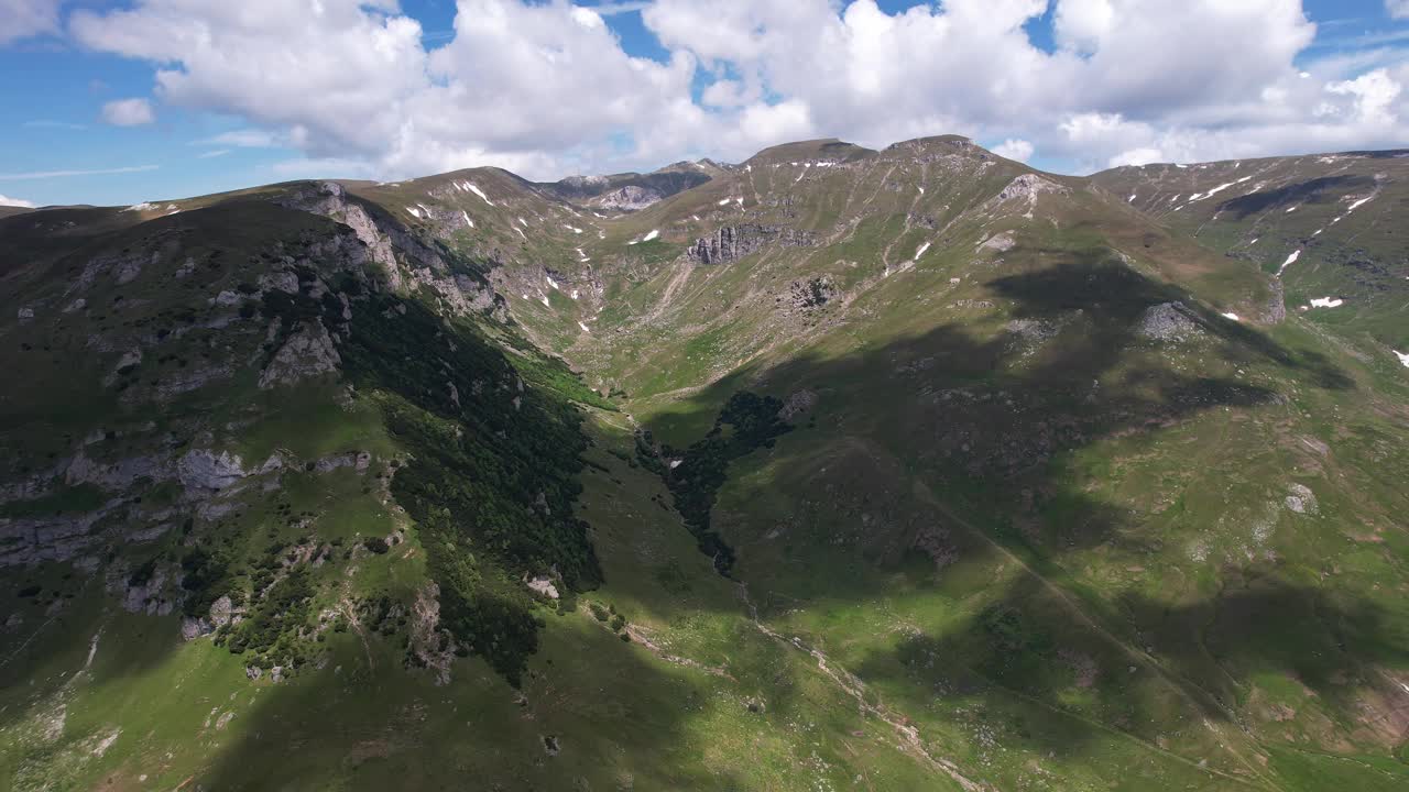 郁郁葱葱的山谷在碧蓝的天空下，阳光沐浴在山丘上，鸟瞰视频素材