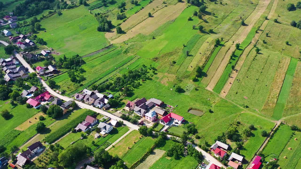 空中拍摄的一个小山村，在一个阳光明媚的日子里，有广阔的绿色田野视频素材