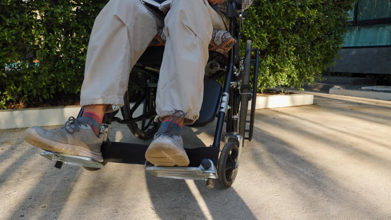 一个残疾的成年妇女，坐在轮椅上，享受着公园小路上的便利和独立，在那里她独自读书。视频下载