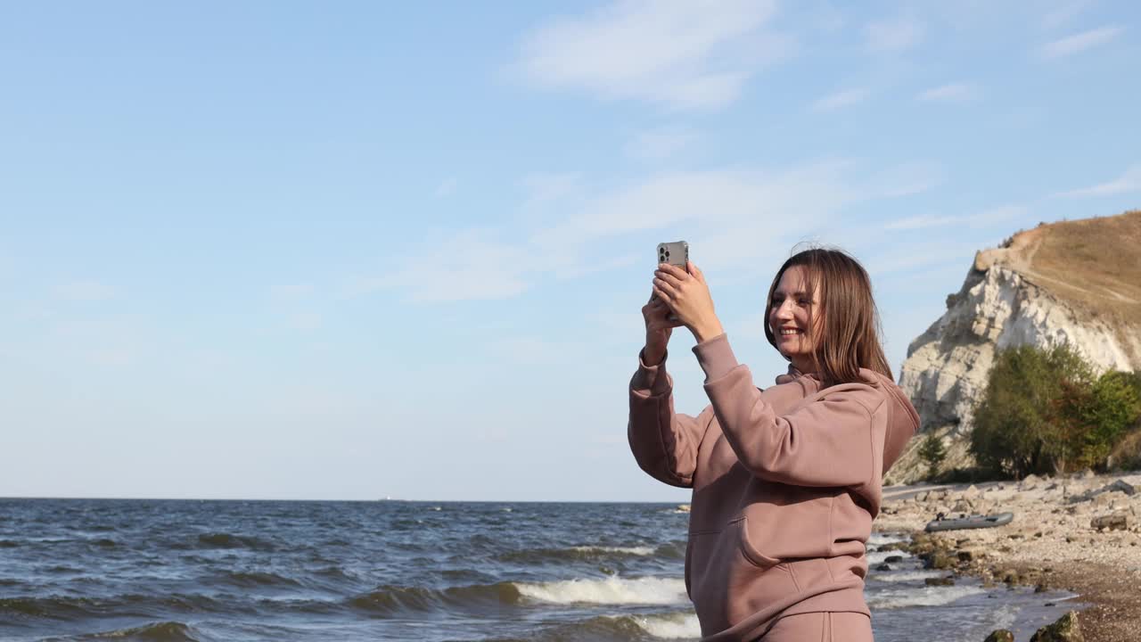 年轻女子用智能手机拍摄海洋、旅游、旅行的美景。视频素材