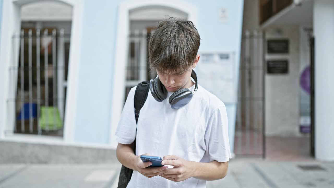 白人少年在城市街道上戴着耳机使用智能手机视频素材