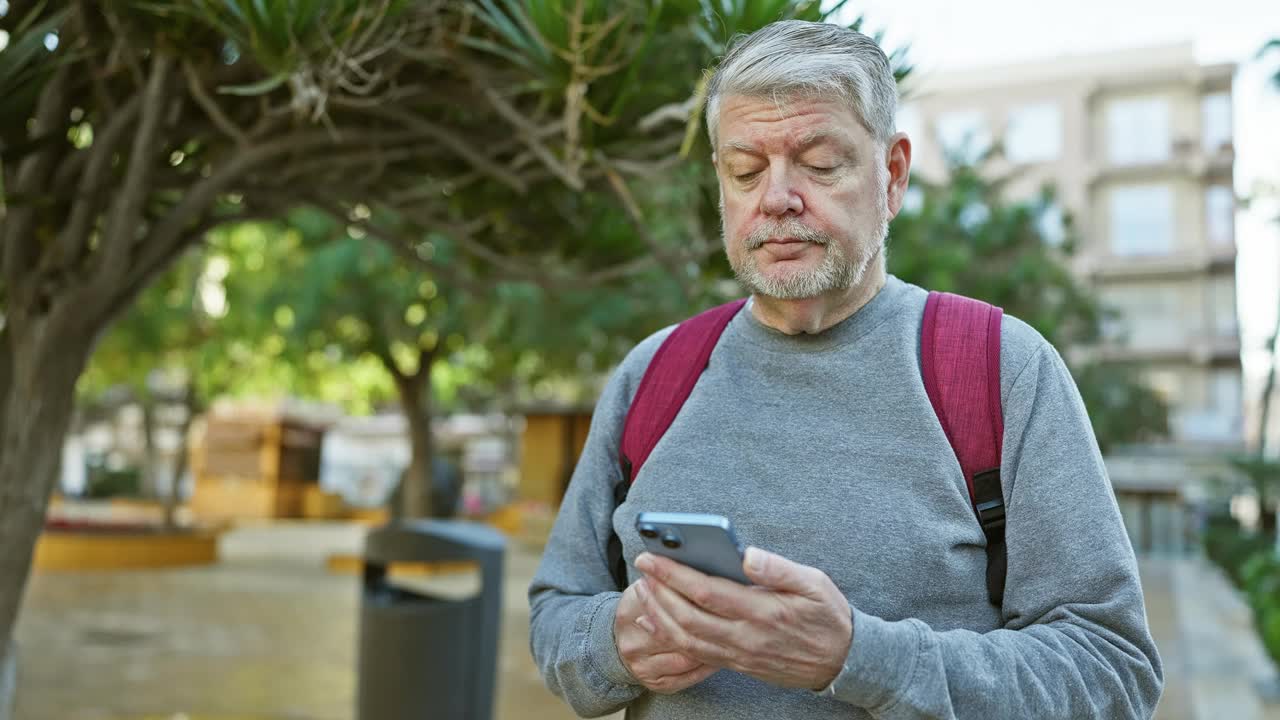 白发苍苍的成熟男子在阳光明媚的城市街道上使用智能手机视频素材