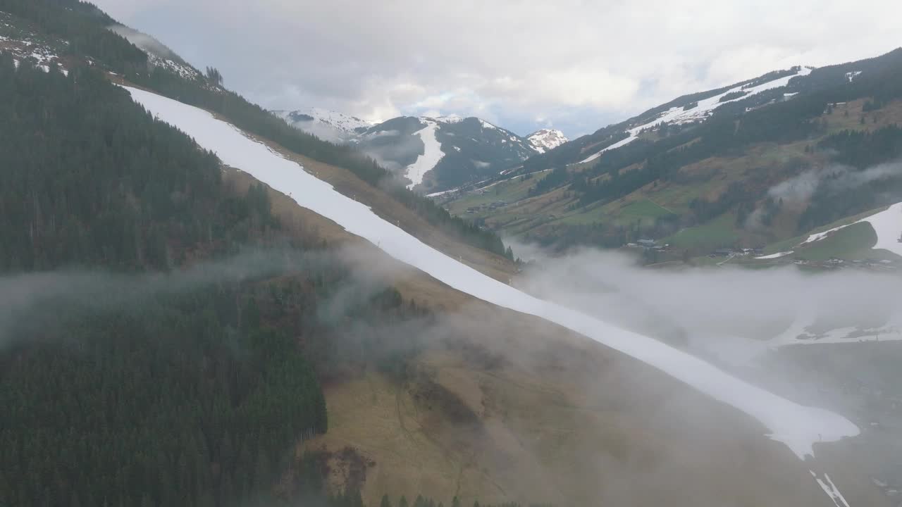 雾笼罩在萨尔巴赫-辛特格勒姆(奥地利)滑雪胜地，白雪皑皑的山脉侧面是绿色的山谷，鸟瞰图视频素材