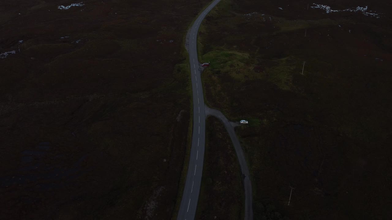 空中无人机在苏格兰斯凯岛穿过山谷的道路上行驶，汽车在乡村田野的天际线与山峰的夕阳下行驶视频素材