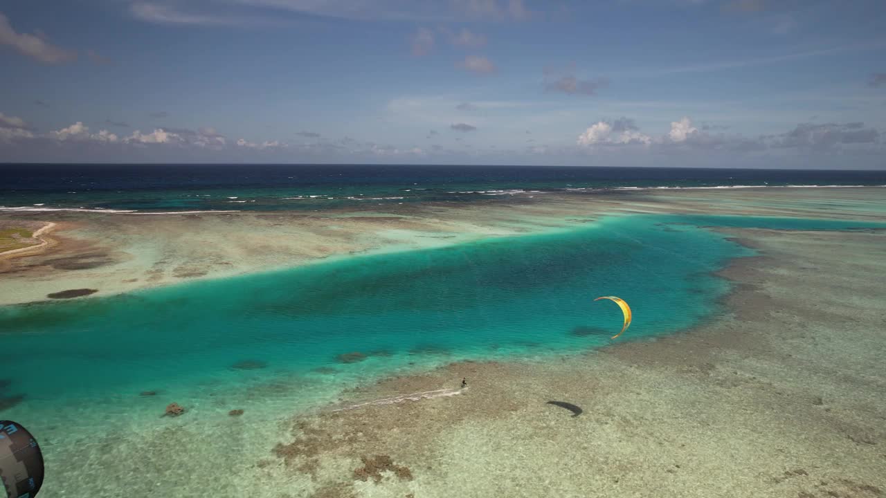 一个风筝冲浪滑翔在清澈的绿松石水域附近的一天，在白天，充满活力和宁静，鸟瞰图视频素材