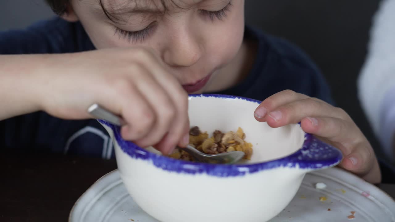 小男孩用勺子在碗里吃麦片。坦率的饥饿的孩子吃小麦食物当早餐视频素材