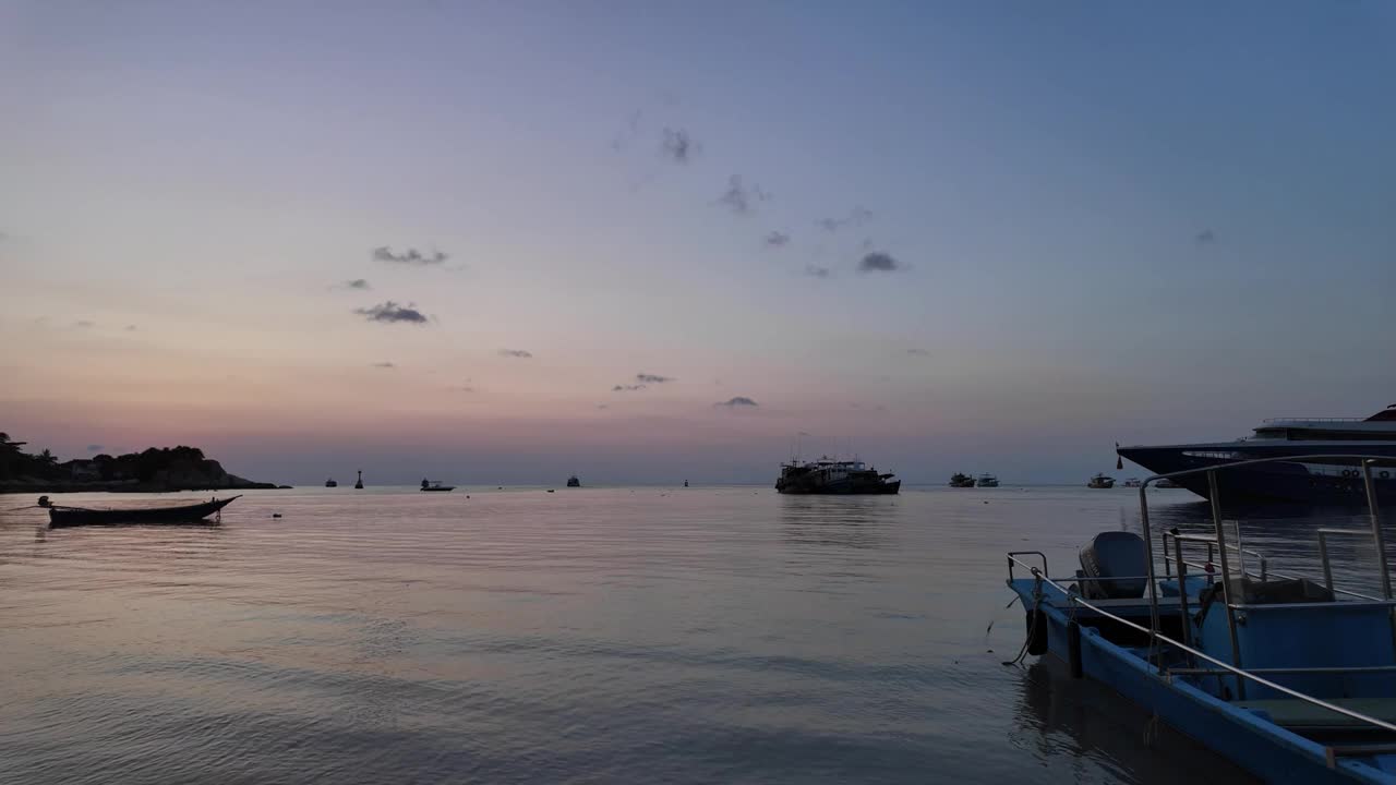 泰国涛岛宁静的水域，宁静的夜晚气氛，渔船轻轻地漂浮在水面上，而远处的游船到达海湾，描绘了一幅宁静的景象。视频素材