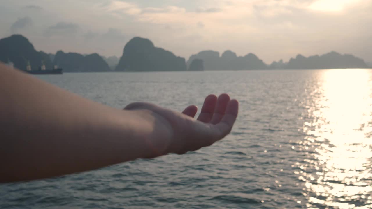 日落时，一只手随着地平线上的下龙湾移动的细节。在越南度假视频下载