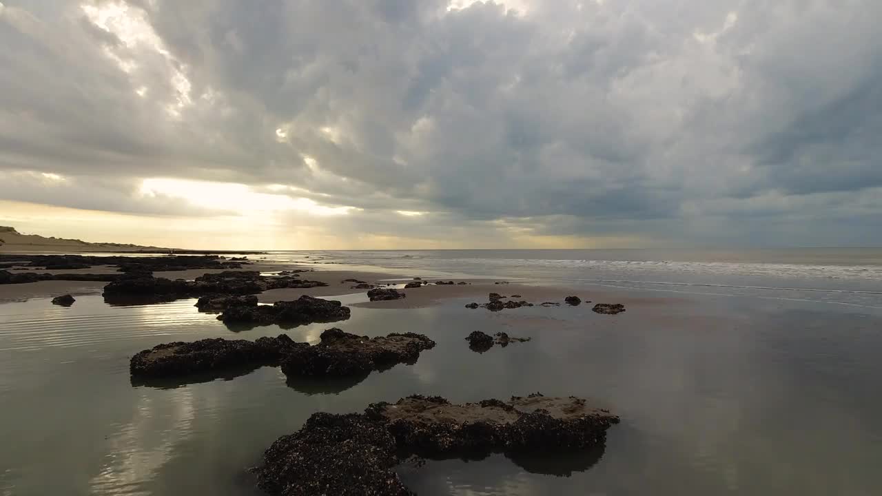 海滩上有岩石、倒影、柔和的海浪、暖色调，天空有美丽的云彩。视频下载