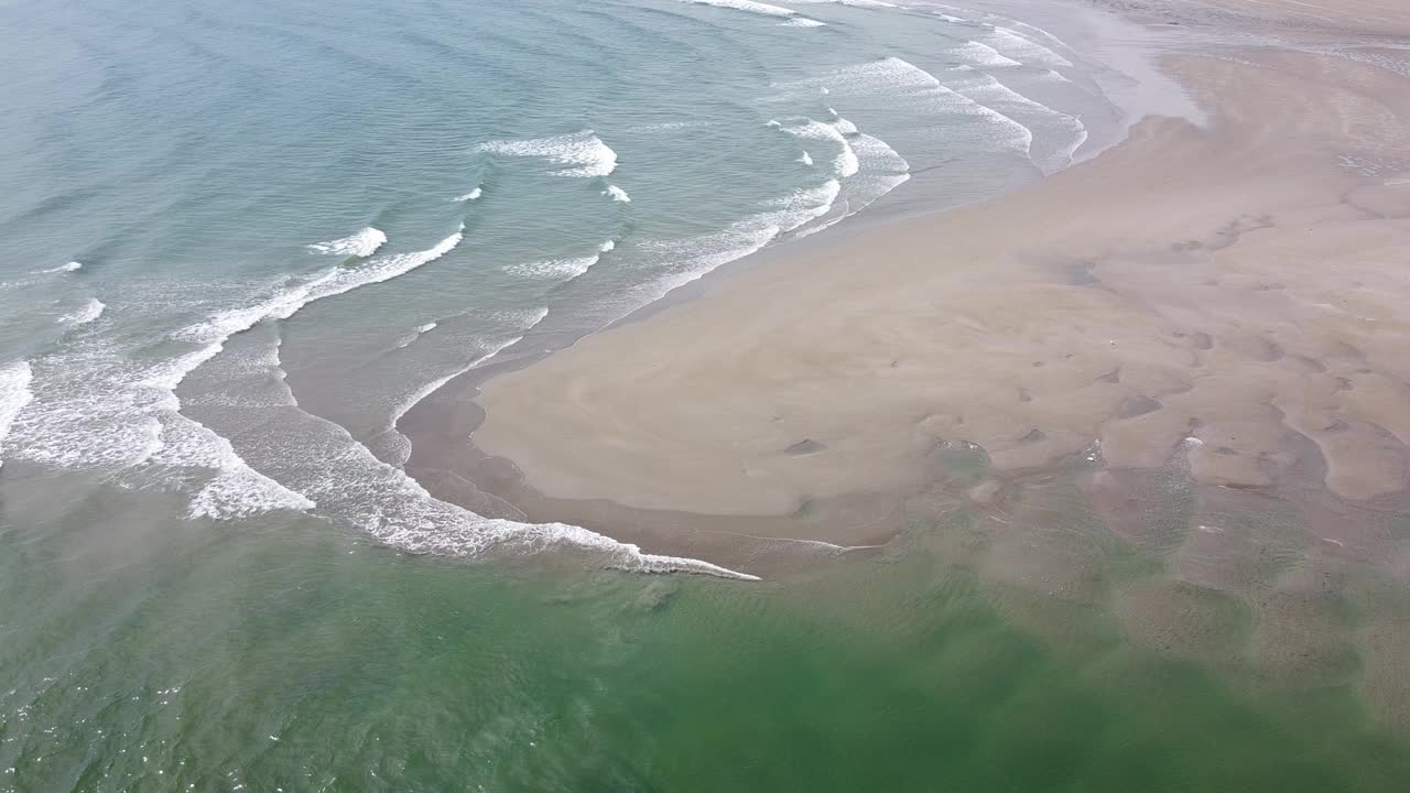 一个荒凉的海滩，有潮湿的沙滩和美丽的海浪。浪花上泛起白色的泡沫。海景俯视图，无人机视频。大西洋表面波涛汹涌，涨潮。视频素材