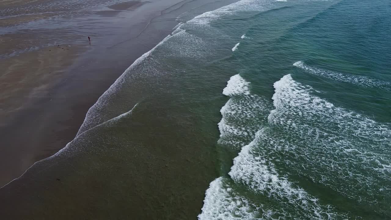 一个荒凉的海滩，有潮湿的沙滩和美丽的海浪。浪花上泛起白色的泡沫。海景俯视图，无人机视频。大西洋表面的波浪。视频素材