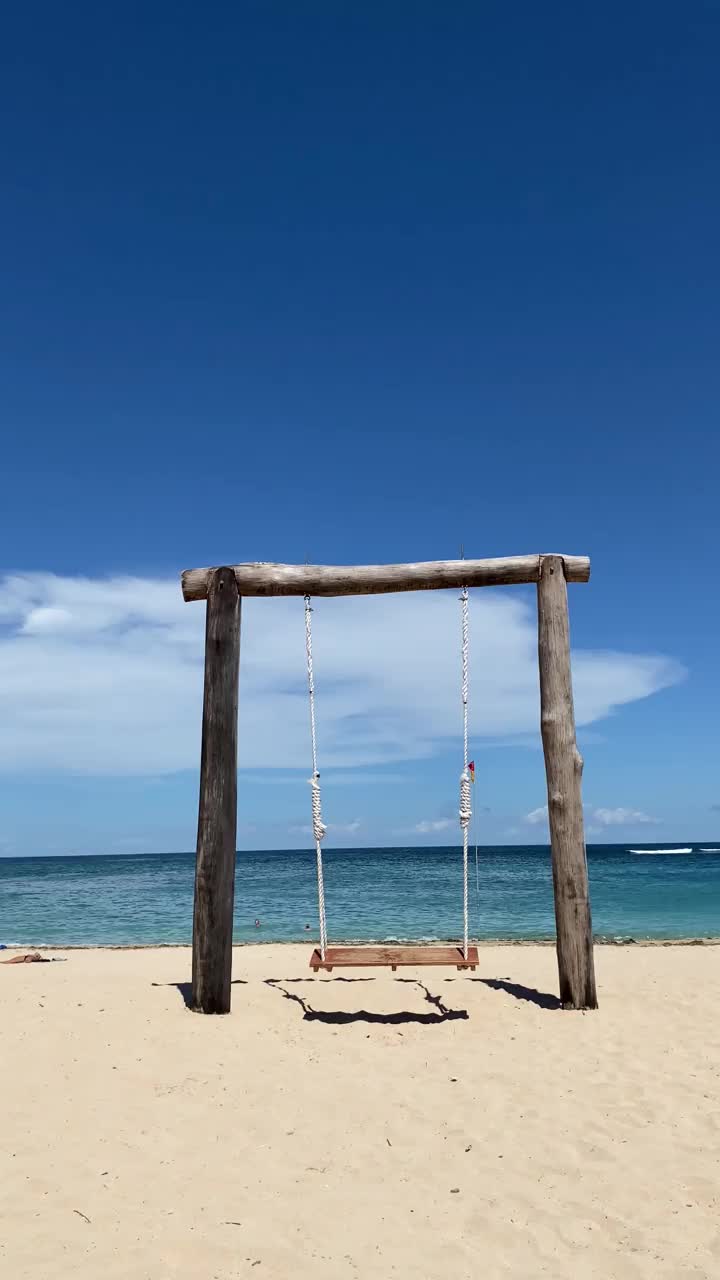 沙滩上的蓝天衬托着空秋千。视频素材