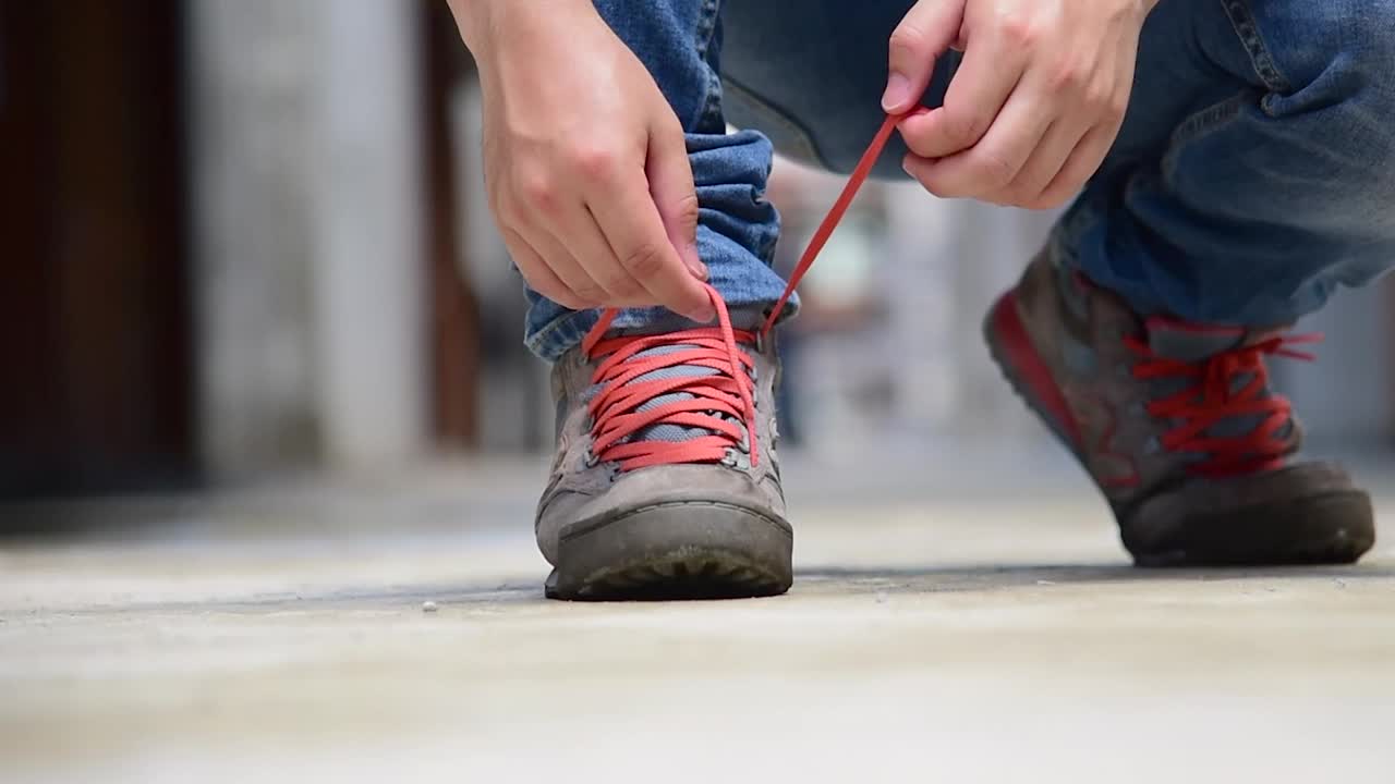 男子跪下来为工人绳系鞋工业靴。近距离拍摄的男子双手系鞋带为他的棕色施工靴。特写男子双手系鞋带为鞋履概念。视频素材