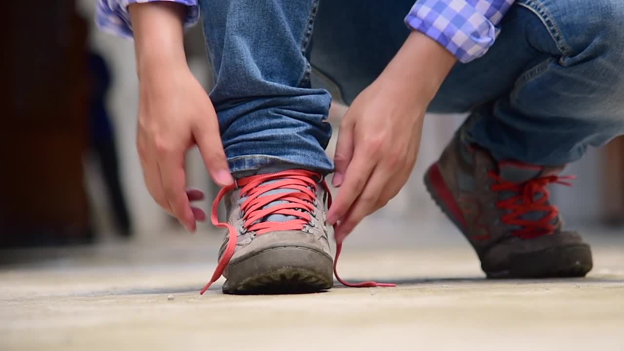 男子跪下来为工人绳系鞋工业靴。近距离拍摄的男子双手系鞋带为他的棕色施工靴。特写男子双手系鞋带为鞋履概念。视频素材