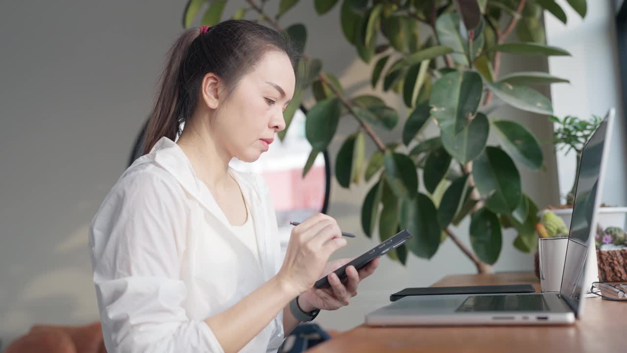 一个女人坐在桌子前，手里拿着笔记本电脑和平板电脑视频素材