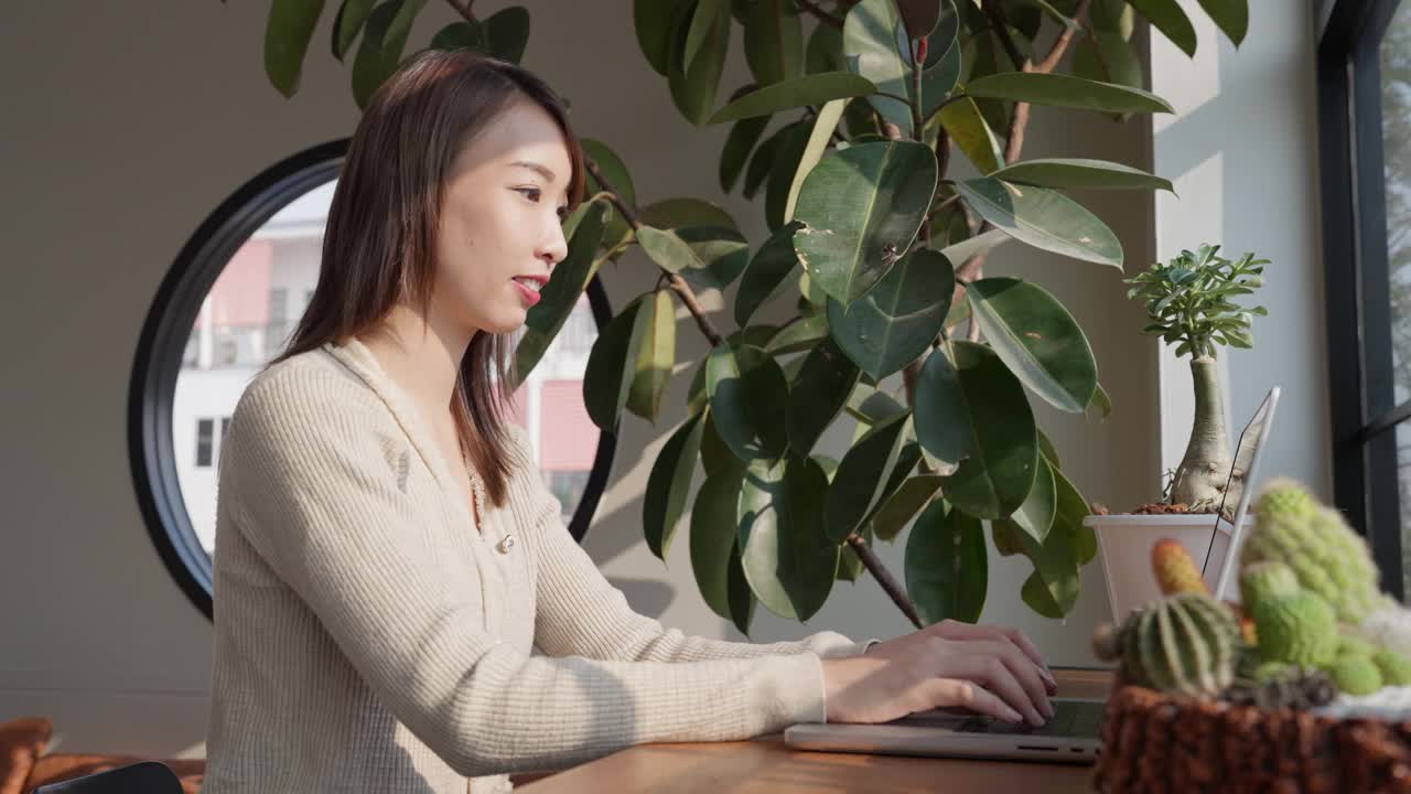 一个女人坐在桌子前，面前放着一台笔记本电脑和一盆植物视频素材