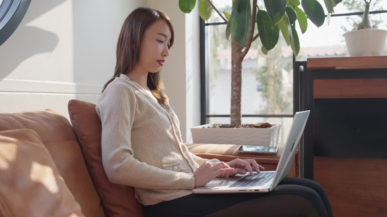一个女人正坐在沙发上用笔记本电脑打字视频素材