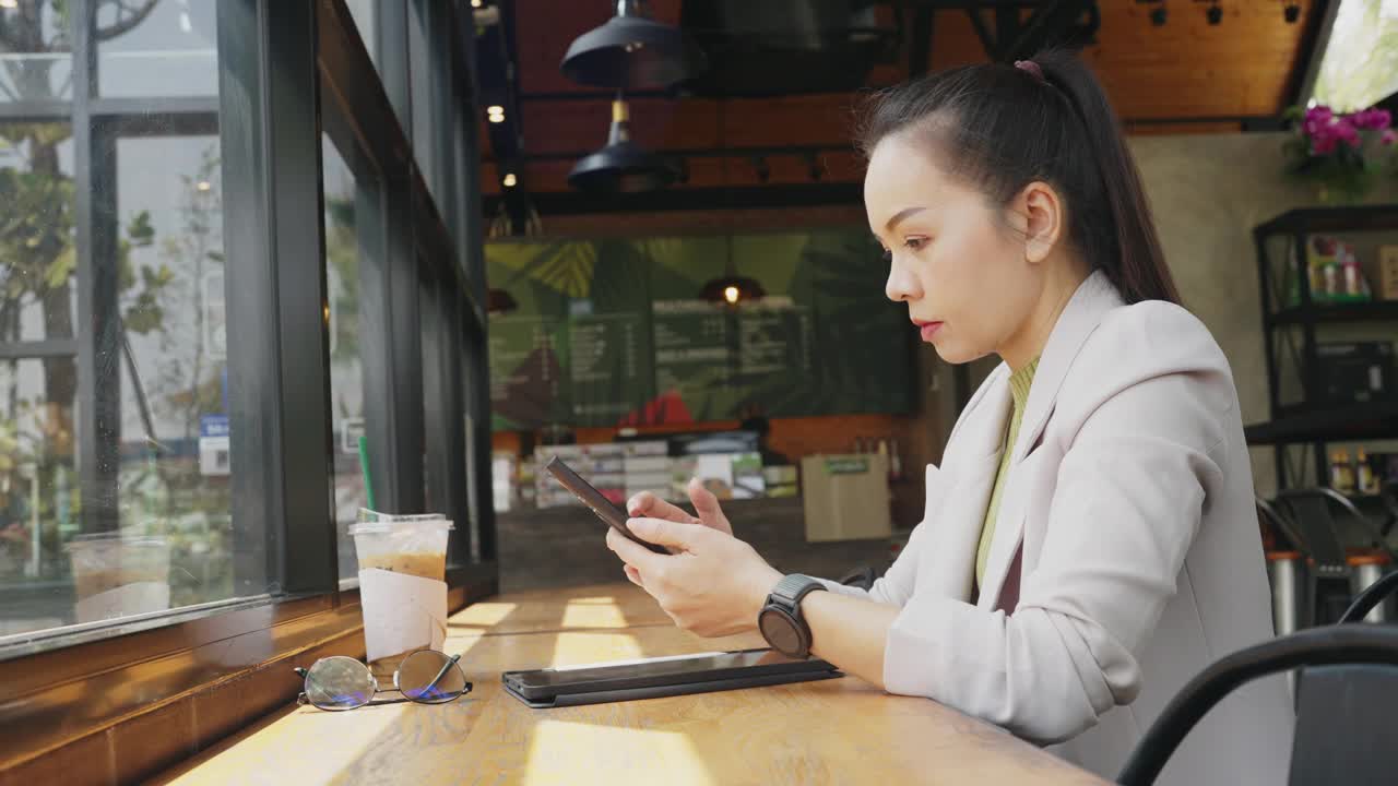 一个女人坐在咖啡馆的桌子旁，看着她的手机视频素材