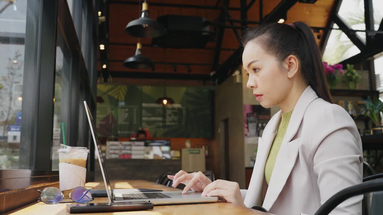 一个女人坐在咖啡馆的桌子旁，在笔记本电脑上打字视频素材