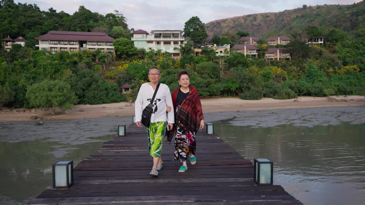 一对退休夫妇在度假时悠闲地手牵手走过一座风景优美的桥。视频下载