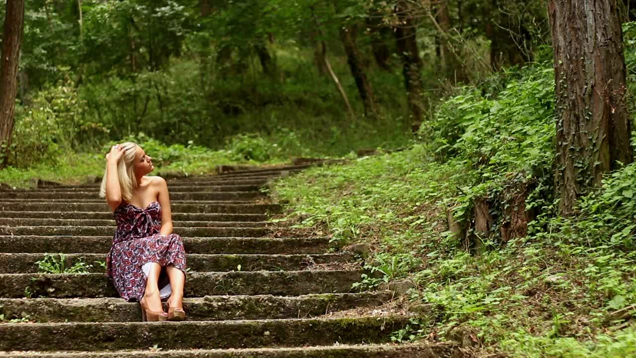 穿着夏日长裙的年轻女子坐在森林里饱经风霜的楼梯上视频素材