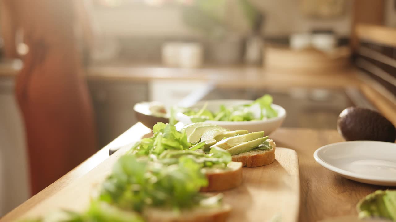 手、牛油果和面包是餐桌上的三明治，沙拉是健康的，饮食和健康是家里的早餐。人们，烤面包和准备水果的营养，素食餐和早餐的食物在家里视频素材