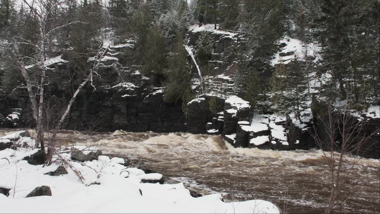 在冬天的暴风雪中，河水沿着岩石峭壁流动视频素材