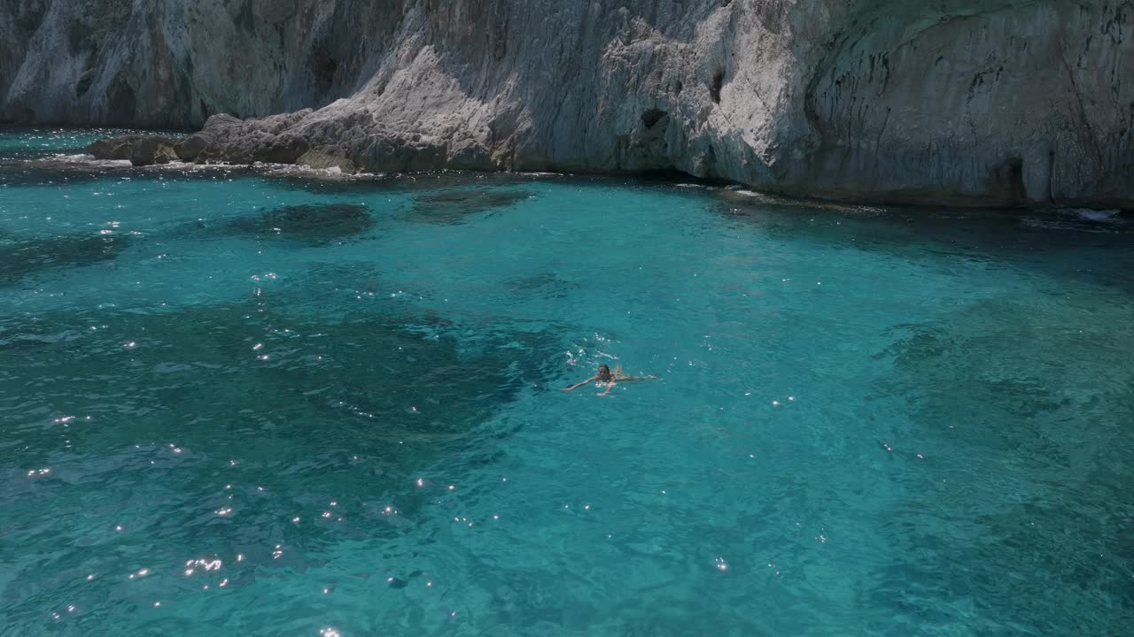 在清澈的海水中游泳的女孩，鸟瞰图，意大利撒丁岛鲍尼海岸视频下载