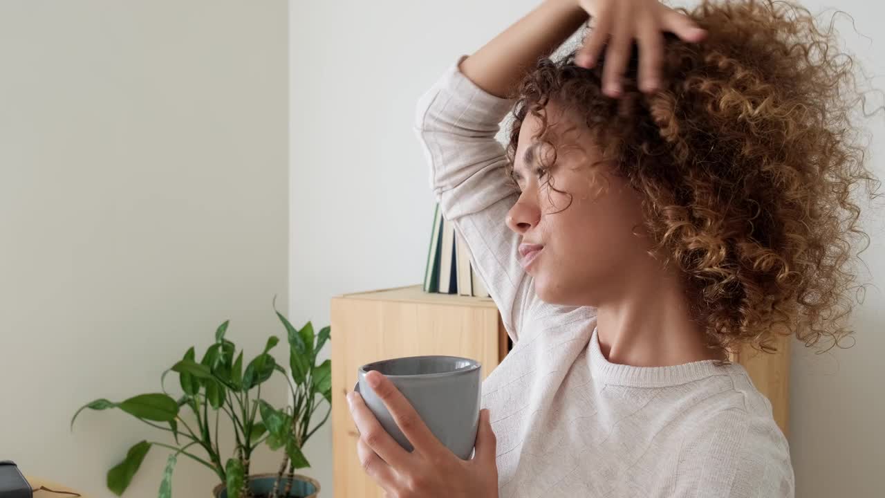 一个多种族的女人在家里休息，一边喝茶，一边看向别处。非裔美国女性在家里喝咖啡。视频素材