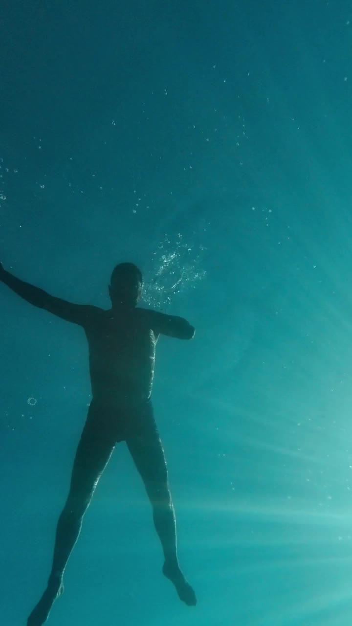 水下拍摄。一个男人正漂浮在水面上，以天空和太阳为背景，看着海底和鱼的垂直视频视频素材